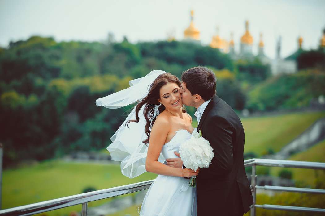 Жених целует невесту, которая держит букет белых цветов - фото 3651433 Фотограф Владимир Лавренчук