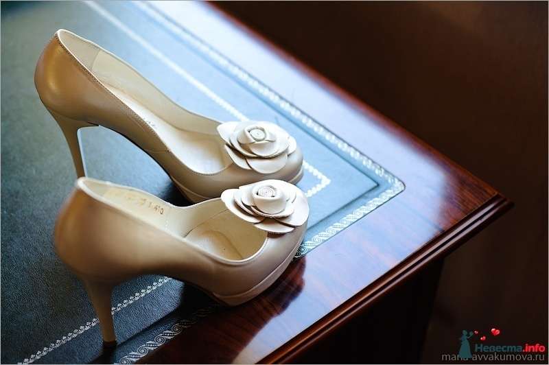 Бежевые туфли на высоком каблуке спереди украшенные декоративным цветком, стоят на столе. - фото 277686 Свадебный фотограф Мария Аввакумова