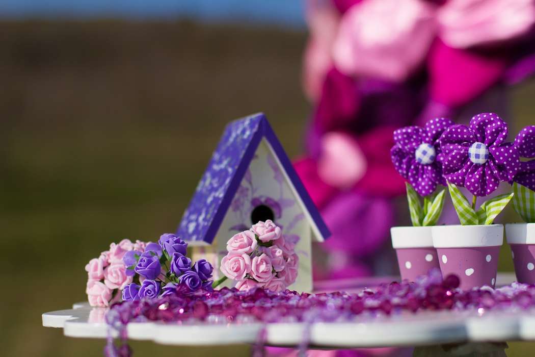 На столике стоят сиреневые горшочки с тканевыми сиреневыми цветами, маленький сиреневый домик и букетики цветов - фото 2233334 Ведущая Егорова Валерия