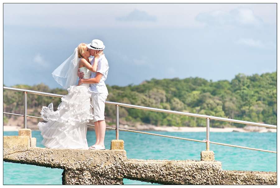 На пляже на мостике жених в белых бриджах, рубашке и шляпе обнимает за талию и целует невесту в белом платье с пышной юбкой, ее - фото 680297 Фотограф на Пхукете Иосиф Юрлов