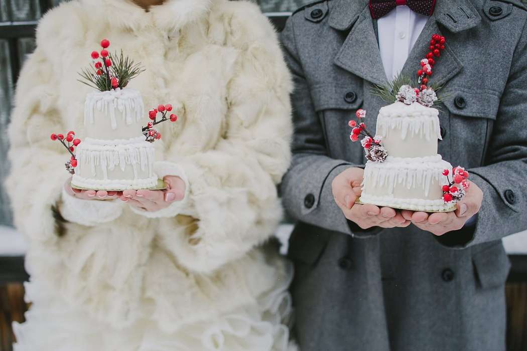 Невеста в белой шубе и жених в сером пальто держат белые свадебные двухъярусные торты, украшенные веточками сосны, шишками, - фото 2657817 Арт-кондитерская "На счастье"