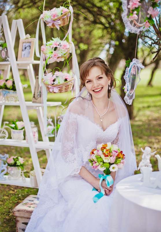 На фоне белой этажерки с букетами цветов и фотографиями,  сидит невеста, держа в руках букет цветов с голубой лентой - фото 2610559 Фотограф Инна Беззубикова