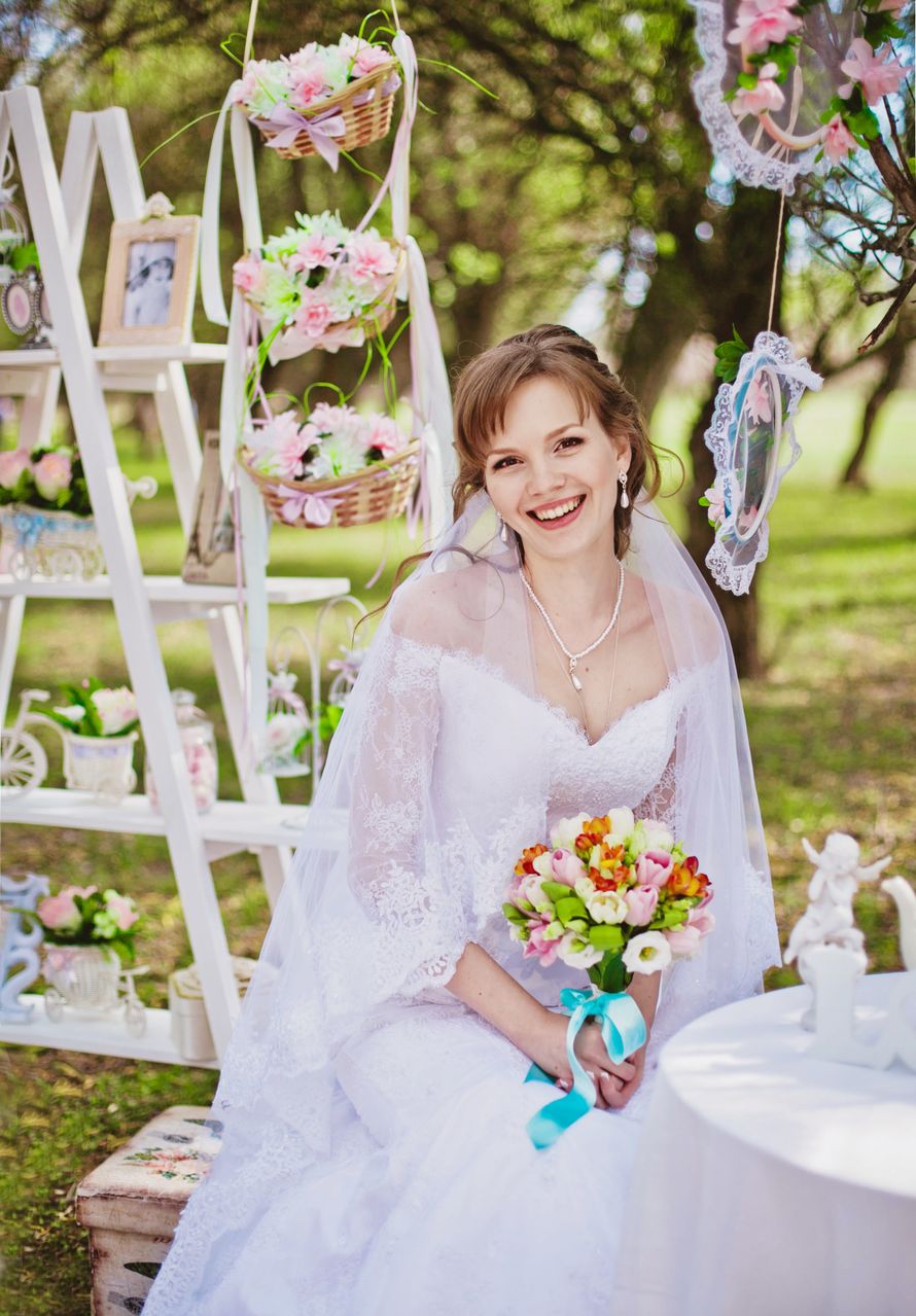 На фоне белой этажерки с букетами цветов и фотографиями,  сидит невеста, держа в руках букет цветов с голубой лентой - фото 2610559 Фотограф Инна Беззубикова