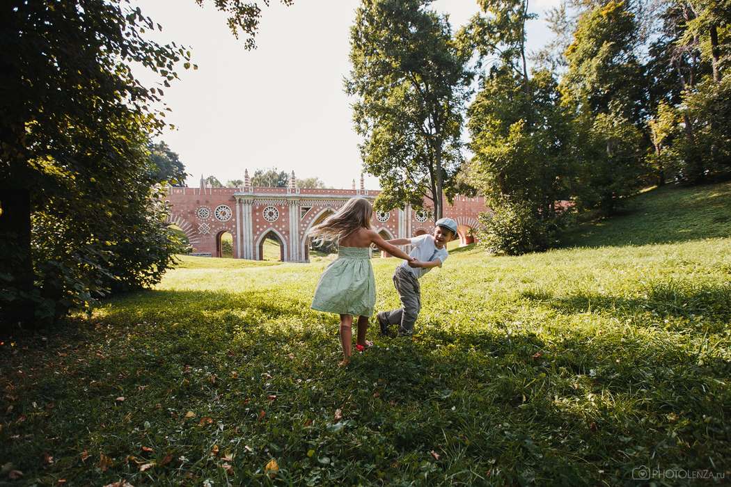 Мальчик и девочка в праздничных нарядах , взявшись за руки бегают на зеленой лужайке рядом со старинным зданием - фото 1563455 Фотограф Елена Защитина