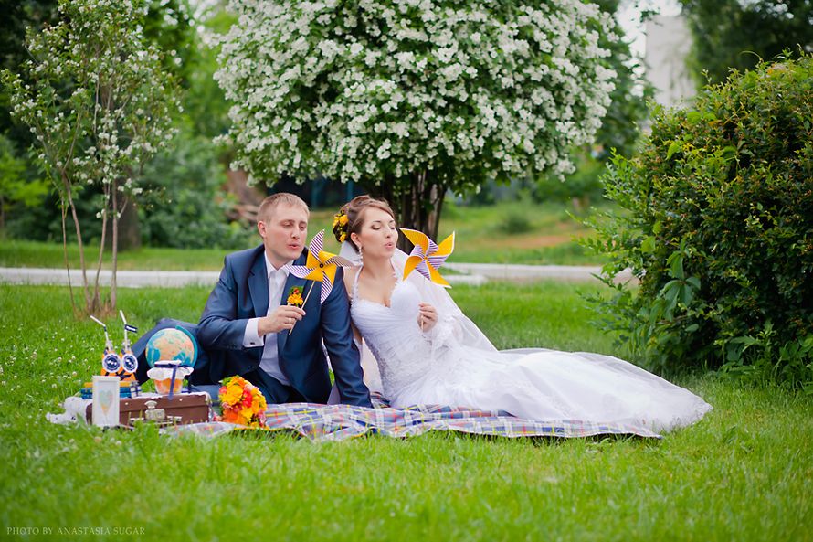 Жених и невеста сидят на клетчатом покрывале между зеленых деревьев и держат в руках жёлтые ветряки  - фото 1067813 Свадебный и семейный фотограф Анастасия Сахарова