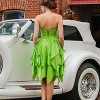 Возле белого ретромобиля подружка невесты в зеленом платье миди с открытой спиной и многоярусной юбкой в бежевых туфлях на шпильке
