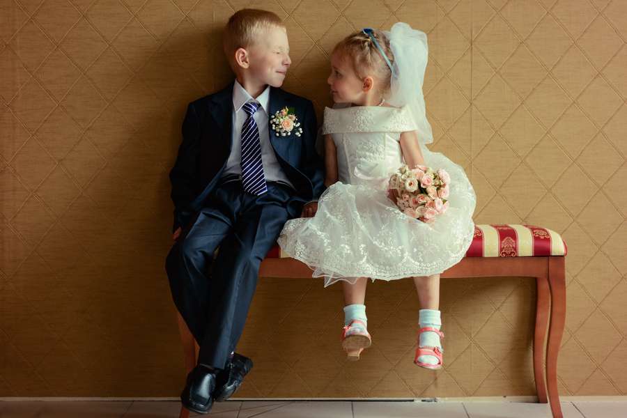 Мальчик в праздничном костюме, украшенный бутоньеркой сидит на красивой деревянной софе рядом с девочкой в белом пышном платье и - фото 1149901 "35 kadrov" - фотосъёмка