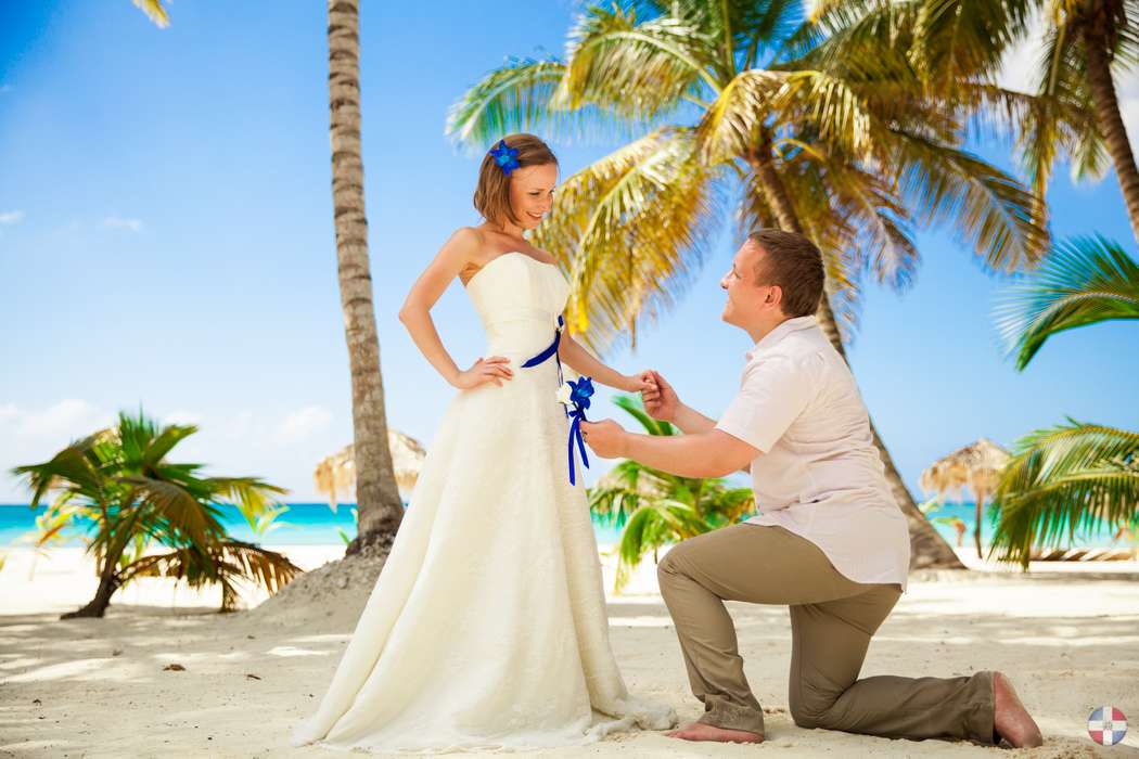 На пляже, жених встал на колено, и дарит невесте голубой цветок, он в белой рубашке и темного цвета брюках, она в белом, открытом - фото 1722171 Аяна2013
