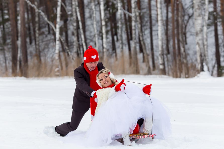 Жених в красной шапке и варежках  толкает сани, на которых сидит невеста в красных варежках - фото 3590825 Студия  "Премьер", фотосъёмка