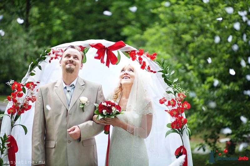 Свадебная арка из живых цветов и  красных лент, на фоне молодоженов - фото 382848 Свадебный организатор Елена - Арт-студия Eventeza