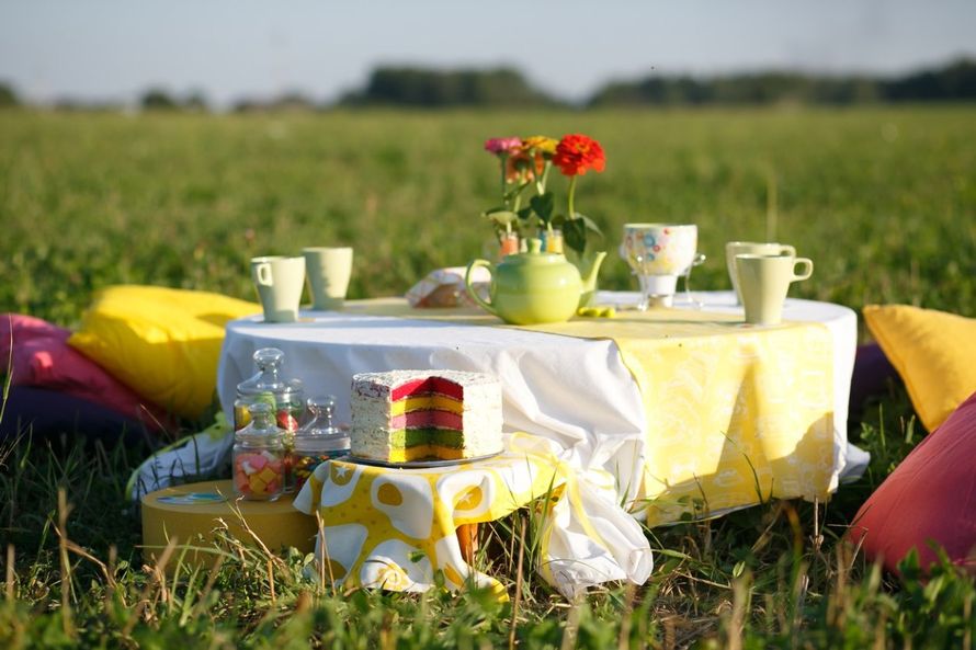 На зеленой траве стоит маленький столик, украшенный жёлтой скатертью, на котором стоят чашки и вазочка с красными цветами - фото 2037874 Мастерская декора и флористики Lemon decor