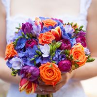Яркий букет невесты из оранжевых роз, красных тюльпанов, сиреневых фрезий, синих гортензий и малиновых пионов