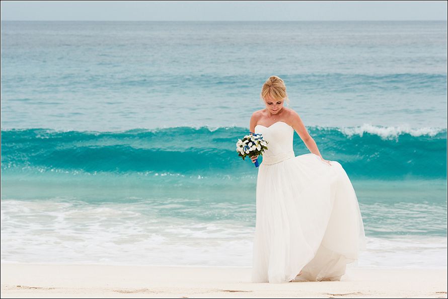По песчаному пляжу гуляет счастливая невеста, на ней открытое белое платье с пышной юбкой, у нее в руке букет из белых и голубых - фото 2384968 Сергей Торгашинов - свадебный фотограф