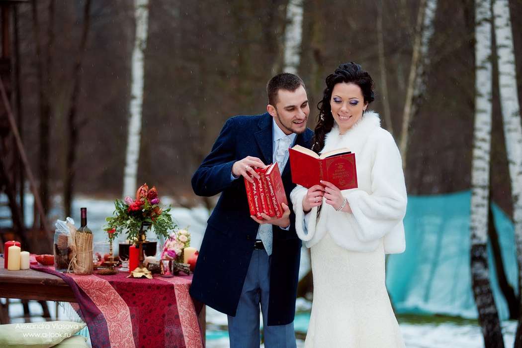 На фоне зимних деревьев, с красными книгами в руках, возле столика, покрытого красной скатертью, стоят жених и невеста - фото 2130360 Винтаж Декор - оформление торжества