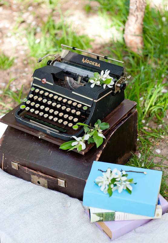 Чёрная печатная машинка на коричневом чехле, рядом книги, украшенные веточками цветущей вишни, фотосессия весенней свадьбы - фото 2465631 Студия декора "Волшебная лавка"