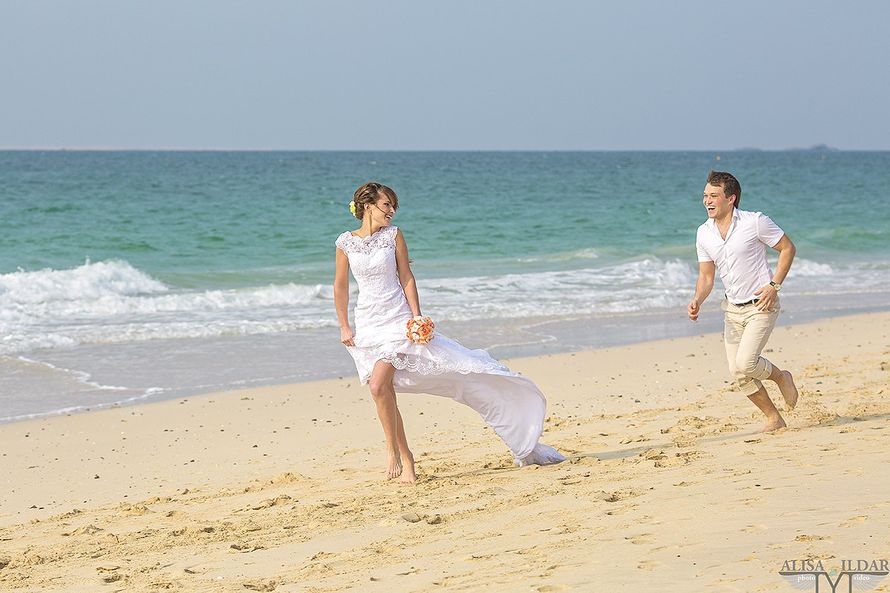 По песчаному пляжу бежит невеста в белом ажурном платье, оглядываясь назад, ее догоняет жених в светлых бриджах и белой рубашке, - фото 2766647 "Tytprod" - фото и видеосъёмка 
