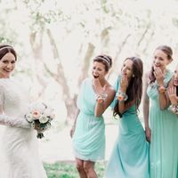 В саду подружки невесты в платьях мятных оттенков коротком и длинных в греческом стиле с цветочными браслетами смотрят на невесту с диадемой в фате, платье с длинным рукавом из гипюра и букетом из белых цветов 