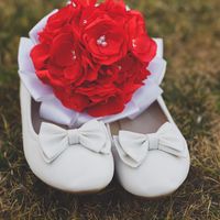 Свадебный букет из красных роз на белых балетках невесты на фоне пожухлой траве