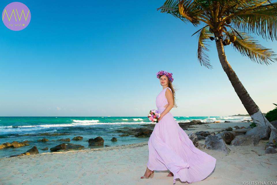 По побережью тропического пляжа идет невеста в сиреневом платье, в руке у нее букет цветов, волосы украшены венком, позади бьется - фото 2915501 My Wish - свадьба и фотосессии в Мексике