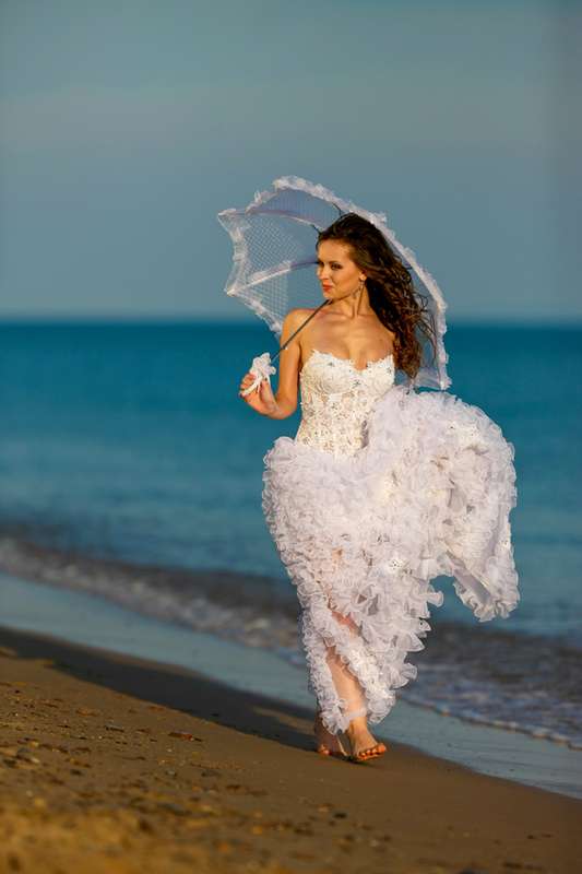 Невеста в красивом ажурном пышном белом платье держит в руке зонтик от солнца прогуливаясь по берегу моря - фото 542973 Фотограф Николай Хорьков
