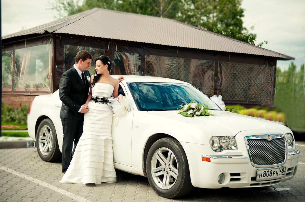 Белый "Chrysler", украшенный экибанами, на фоне летней беседки, рядом с новобрачными. - фото 532514 Прокат авто Chrysler 300С
