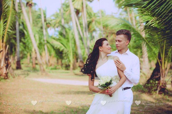 На тропическом пляже стоит влюбленная пара, жених в легком белом костюме нежно обнимает за плечи невесту в белом платье, она - фото 2832691 Romantica - свадебное агентство в Таиланде
