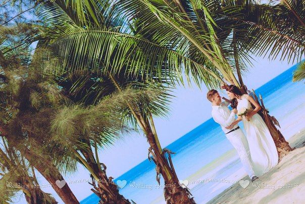 На песчаном пляже в тени тропических деревьев стоят молодожены, глядя друг другу в глаза, жених в белом легком костюме, невеста в - фото 2832695 Romantica - свадебное агентство в Таиланде