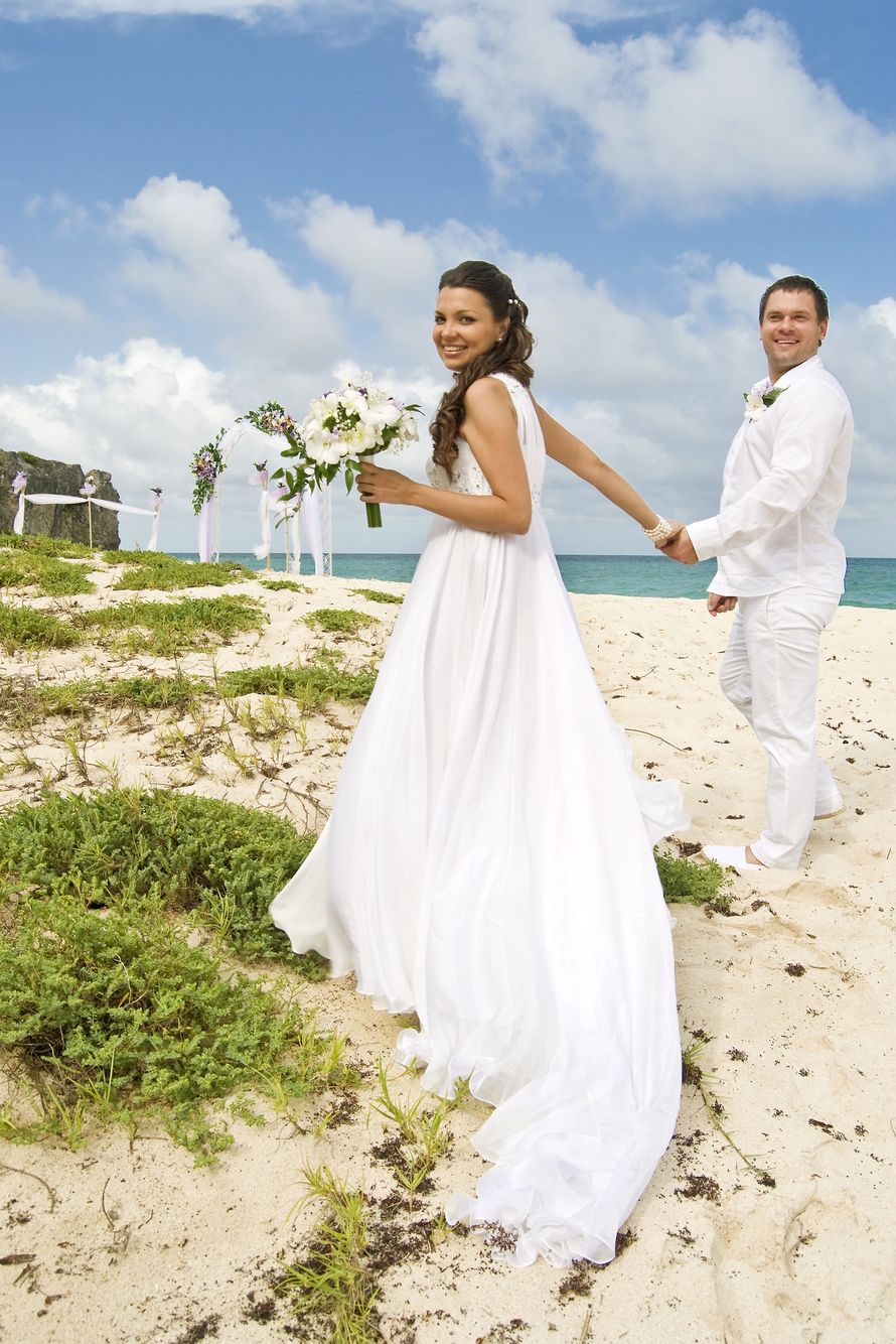 На природе, на пляже, стоят жених и невеста, держась за руки, он в белой рубашке и белых брюках, она в белом, длинном платье, со - фото 1536605 Lesech'ka