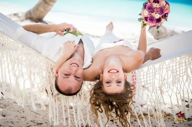 На пляже лежат в гамаке жених с невестой, она в белом, длинном платье с букетом цветов, он в белой рубашке и брюках - фото 2811215 Caribbean Wedding - свадьба в Доминикане