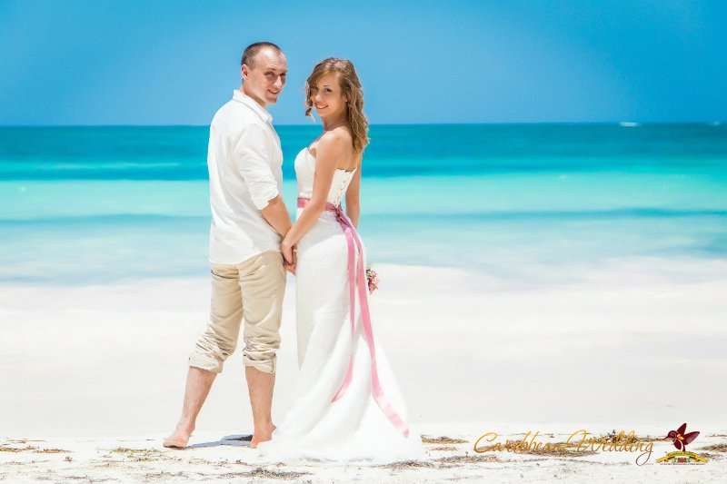 На песчаном пляже на фоне лазурного океана стоит влюбленная пара, держась за руки, жених в светлых бриджах и белой рубашке, - фото 2811219 Caribbean Wedding - свадьба в Доминикане