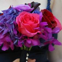 Яркий букет невесты из ярко-красных и розовых роз, синих гортензий и ярко-сиреневых орхидей, декорированный темно-синей лентой и белыми бусинами 